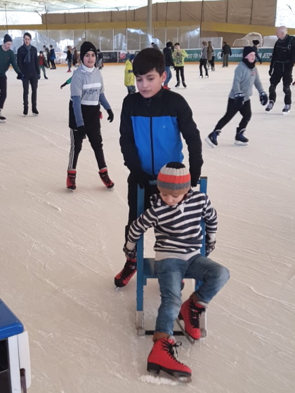 Junge schiebt weiteren Jungen auf Stuhl übers Eis