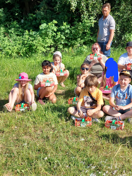 Kinder sitzen vor dem Sensei im Gras und präsentieren ihre gefüllten Sammelkörbe