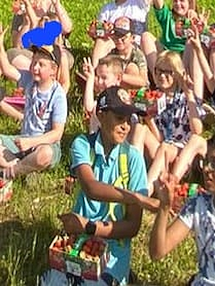 Kinder sitzen mit ihren gefüllten Sammelkörben im Gras und machen das Victory-Zeichen