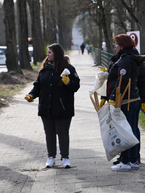Zwei Frauen auf dem Gehweg mit Pappbecher und Müllsack