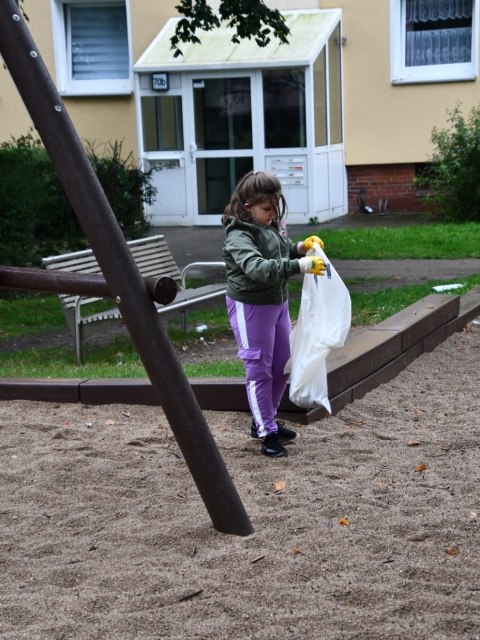 Mädchen mit Müllsack auf Spielplatz vor Wohnhaus